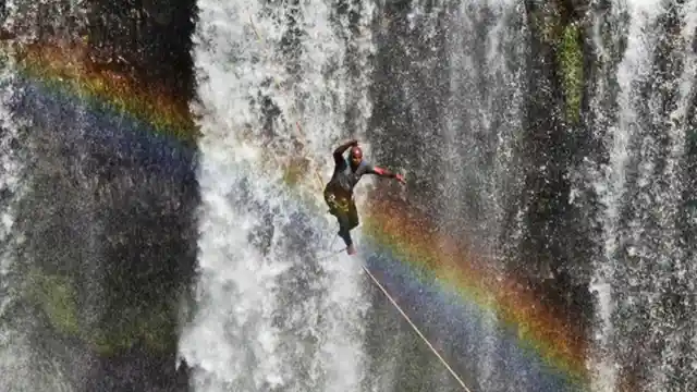 Man Tightroping Through Rainbow Above Waterfall